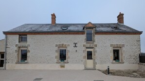 Un edificio de piedra de dos pisos con una fachada simétrica, que presenta una puerta central y dos ventanas en cada planta.