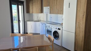 A modern kitchen with wooden cabinets, a white refrigerator, a built-in oven, a washing machine, and a dining area with a glass table and wicker chairs. - Modern Duplex in the Heart of Jaca for 6 People (Jaca)