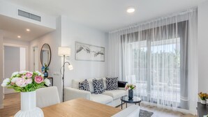 A modern living room with a wooden dining table, a sofa set, and a large window with sheer curtains. - Modern apartment in Estepona with parking, near beaches (Estepona)