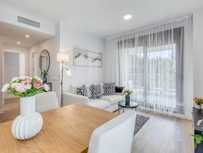 A modern living room with a wooden dining table, a sofa set, and a large window with sheer curtains. - Modern apartment in Estepona with parking, near beaches (Estepona)