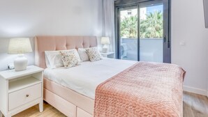 A bedroom with a bed, nightstands, a window with a view, and a door. - Modern apartment in Estepona with parking, near beaches (Estepona)