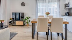 A modern living room with a flat-screen TV, a dining table with chairs, a clock on the wall, and a kitchen area with a microwave. - Modern apartment in Estepona with parking, near beaches (Estepona)