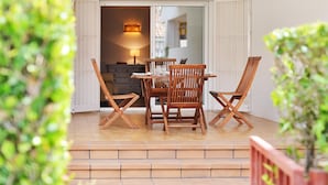Un patio con una mesa y sillas de madera, una puerta corrediza de vidrio que da a un espacio interior y una planta pequeña en primer plano.