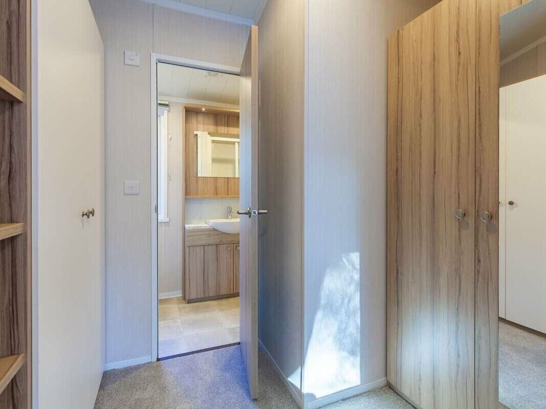 Ein Flur, der zu einem Badezimmer mit Holztür und Spiegel führt.