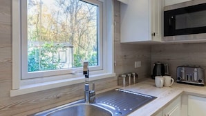 A modern kitchen with a stainless steel sink, a window overlooking a garden, a microwave, and a toaster. - Azenor Lodge - Kelling Heath Holiday Park - 16221 (Holt)