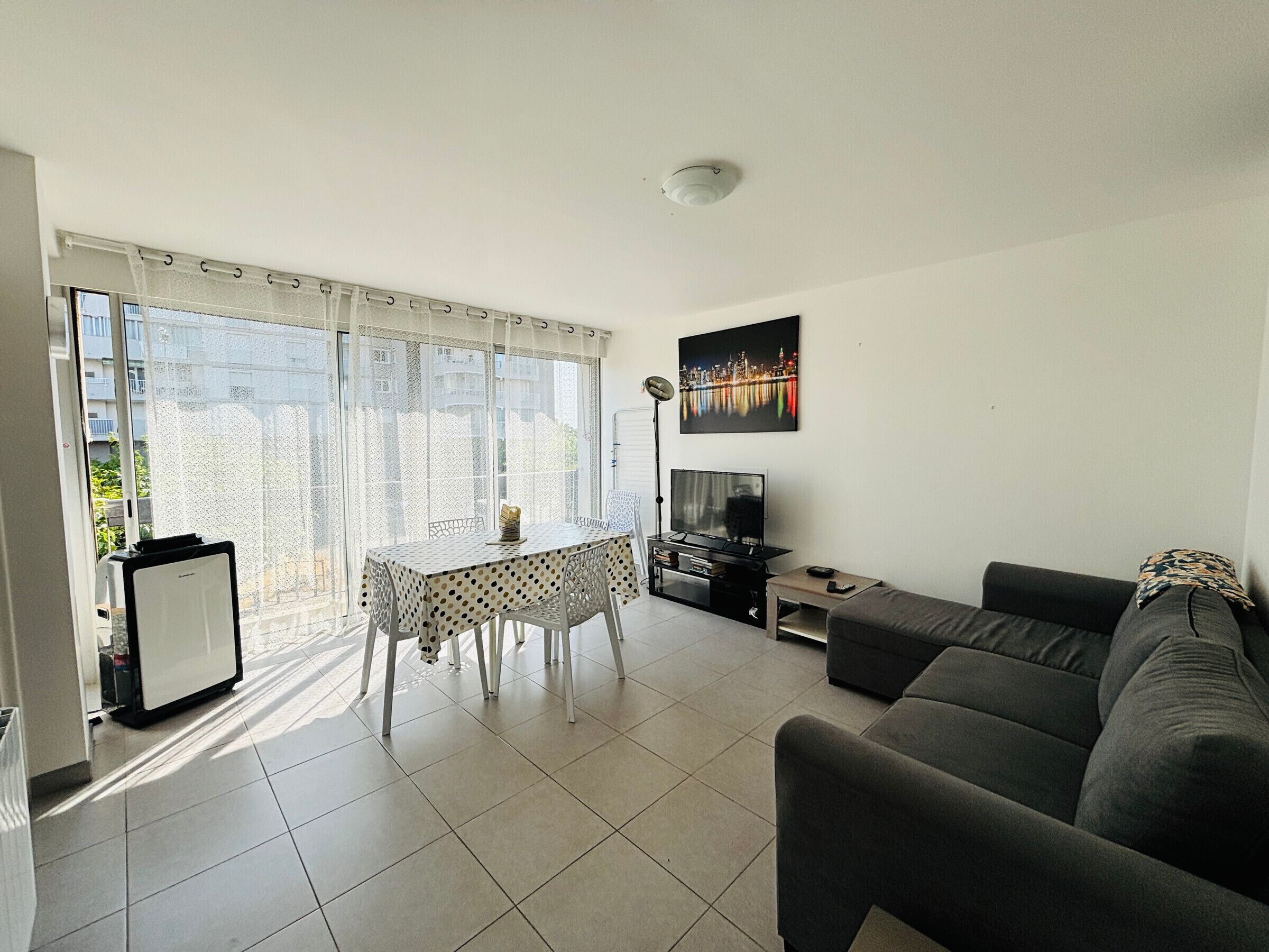 Ein Wohnzimmer mit einer Couch, einem Fernseher, einem Esstisch mit Stühlen und einem Stadtbild.