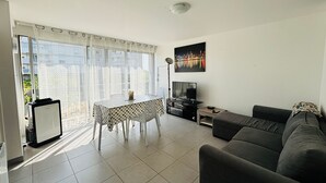 Una sala de estar con sofá, televisión, una mesa de comedor con sillas y un cuadro de un paisaje urbano.