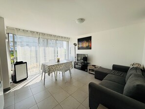 Ein Wohnzimmer mit einer Couch, einem Fernseher, einem Esstisch mit Stühlen und einem Stadtbild.