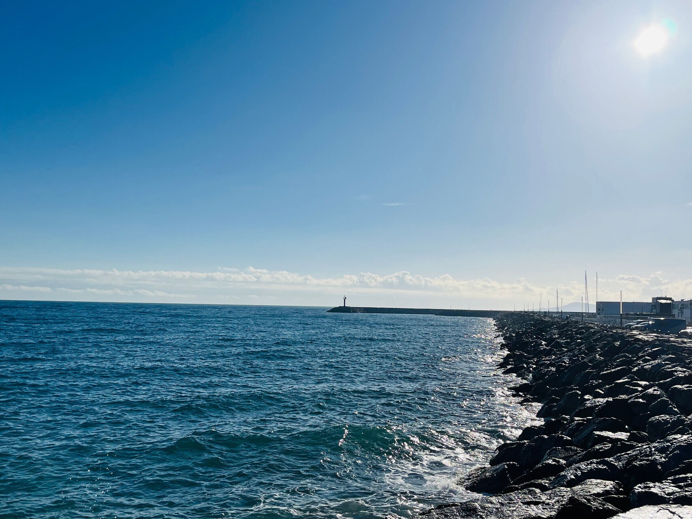 Eine Küstenansicht mit felsiger Küste, einem Leuchtturm in der Ferne und blauem Himmel.