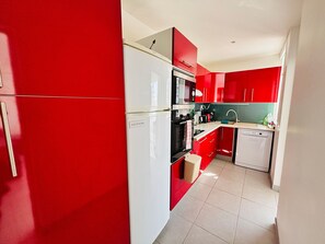 A modern kitchen with red cabinetry, stainless steel appliances, and a tiled floor. - Saint-Cyprien: Modern T3 near beach with private parking (Saint-Cyprien)
