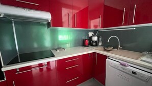 Una cocina con armarios rojos, encimera blanca, estufa y lavavajillas.