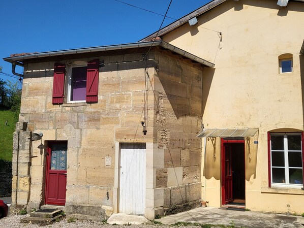 A two-story stone building with red shutters and a white door.