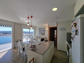 A modern kitchen with a central island, white chairs, and a view of the sea through large windows. - Charming apartment 100m from beach with terrace and pool (L'Escala)
