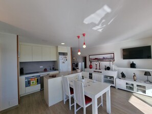 A modern kitchen with white cabinets, a dining area with a white table and chairs, and a TV mounted on the wall. - Charming apartment 100m from beach with terrace and pool (L'Escala)