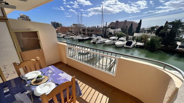 Un balcón con una mesa lista para dos, con vista a un puerto deportivo y barcos.