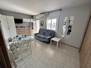 A compact living space with a dining area, a sofa, and a TV mounted on the wall. - Comfortable studio with AC and Wi-Fi, 800m from Santa Margarita beach (Roses)
