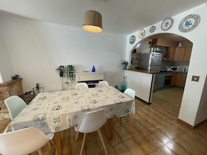 A dining area with a table set for four, a kitchen with modern appliances, and decorative plates on the wall. - Charming Apartment in Puig Rom, Roses with Parking and Terrace, Sleeps 8 (Roses)