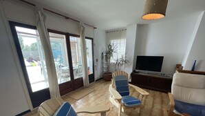 A living room with a TV, two blue chairs, a patterned ottoman, and a wooden table. - Charming Apartment in Puig Rom, Roses with Parking and Terrace, Sleeps 8 (Roses)