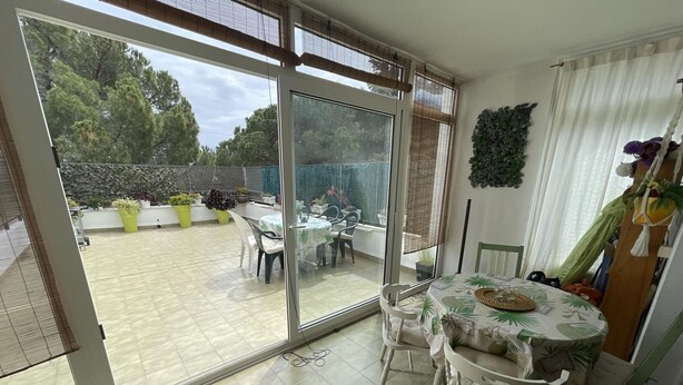 A patio with a table and chairs, a sliding glass door leading to a garden, and a view of trees and plants. - Charming Apartment in Puig Rom, Roses with Parking and Terrace, Sleeps 8 (Roses)