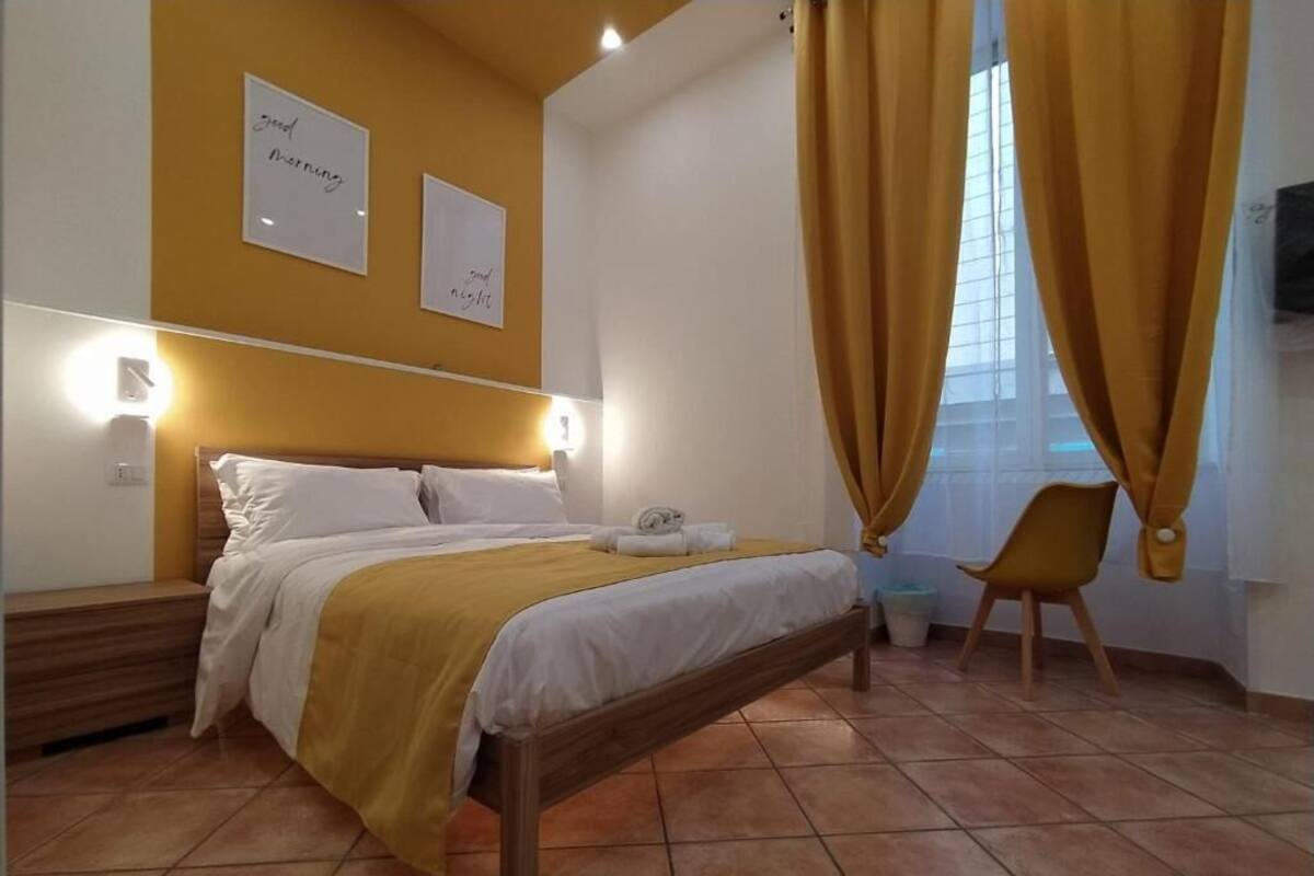 Une chambre à coucher avec un lit, une table de chevet, une chaise et une fenêtre avec des rideaux.