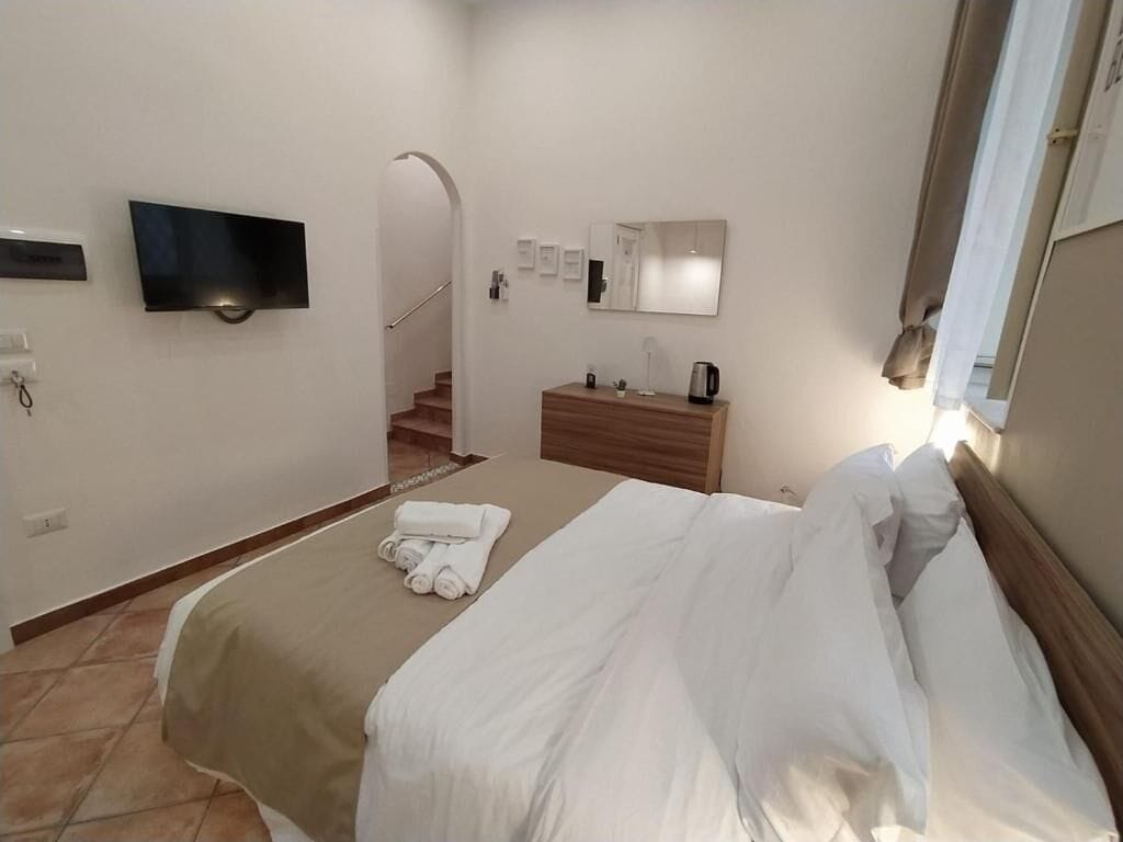 A hotel room with a bed, a TV mounted on the wall, a wooden dresser, and a mirror.