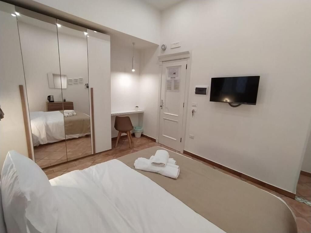 A hotel room with a bed, a desk, a chair, a TV, and a wardrobe.