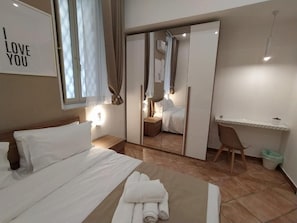 Habitación de hotel con cama, escritorio, silla, espejo y cartel en la pared.