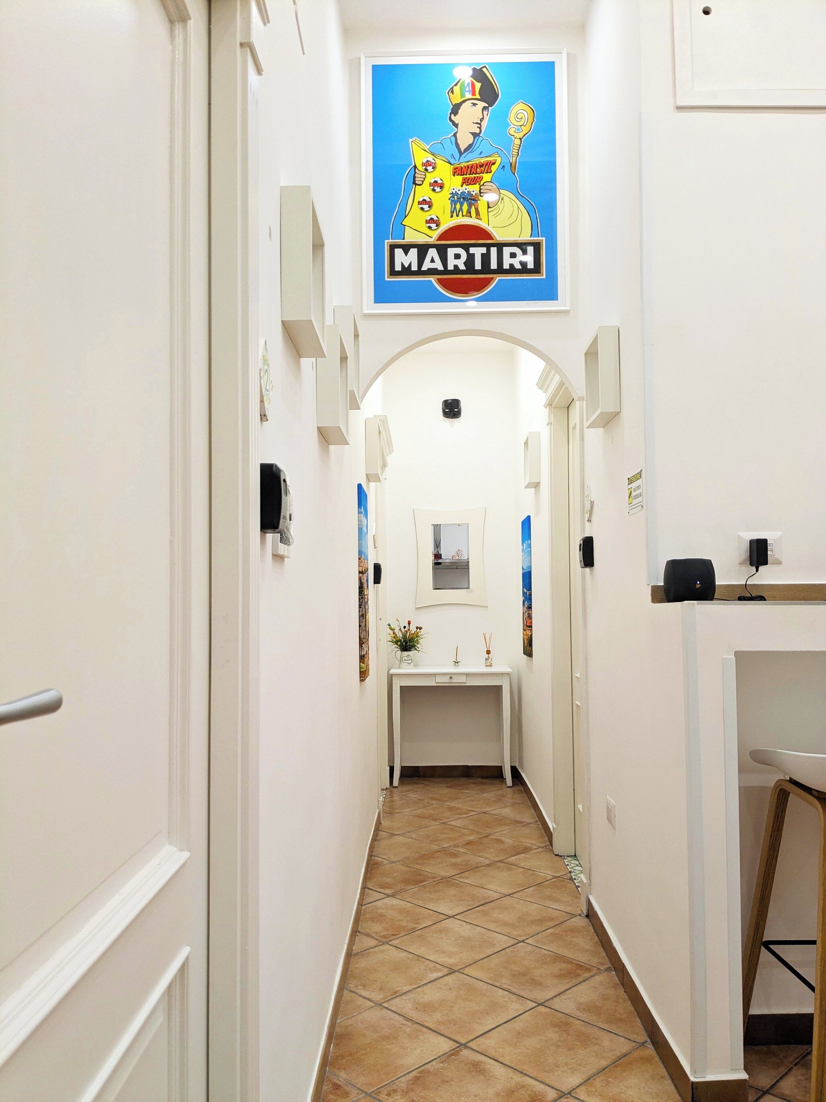 A narrow hallway with a tiled floor, a white console table with a mirror and a small plant, and a poster of a man holding a sign that reads "MARTINI."