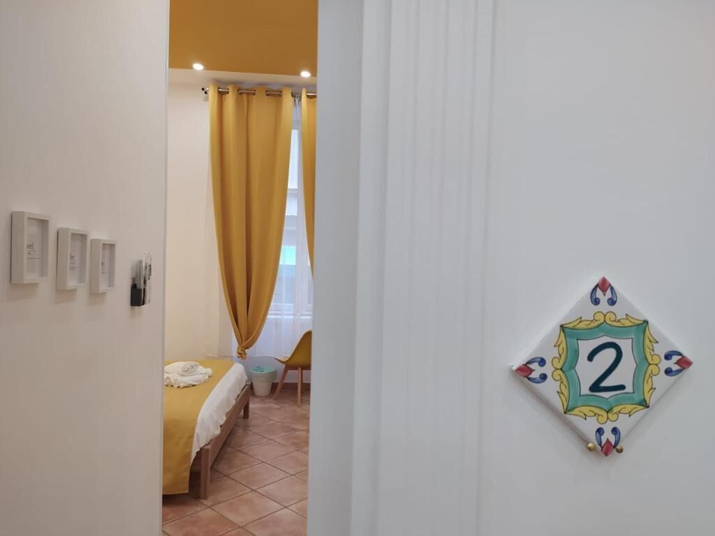 A hotel room with a bed, a small table, a chair, and a number plaque on the wall.