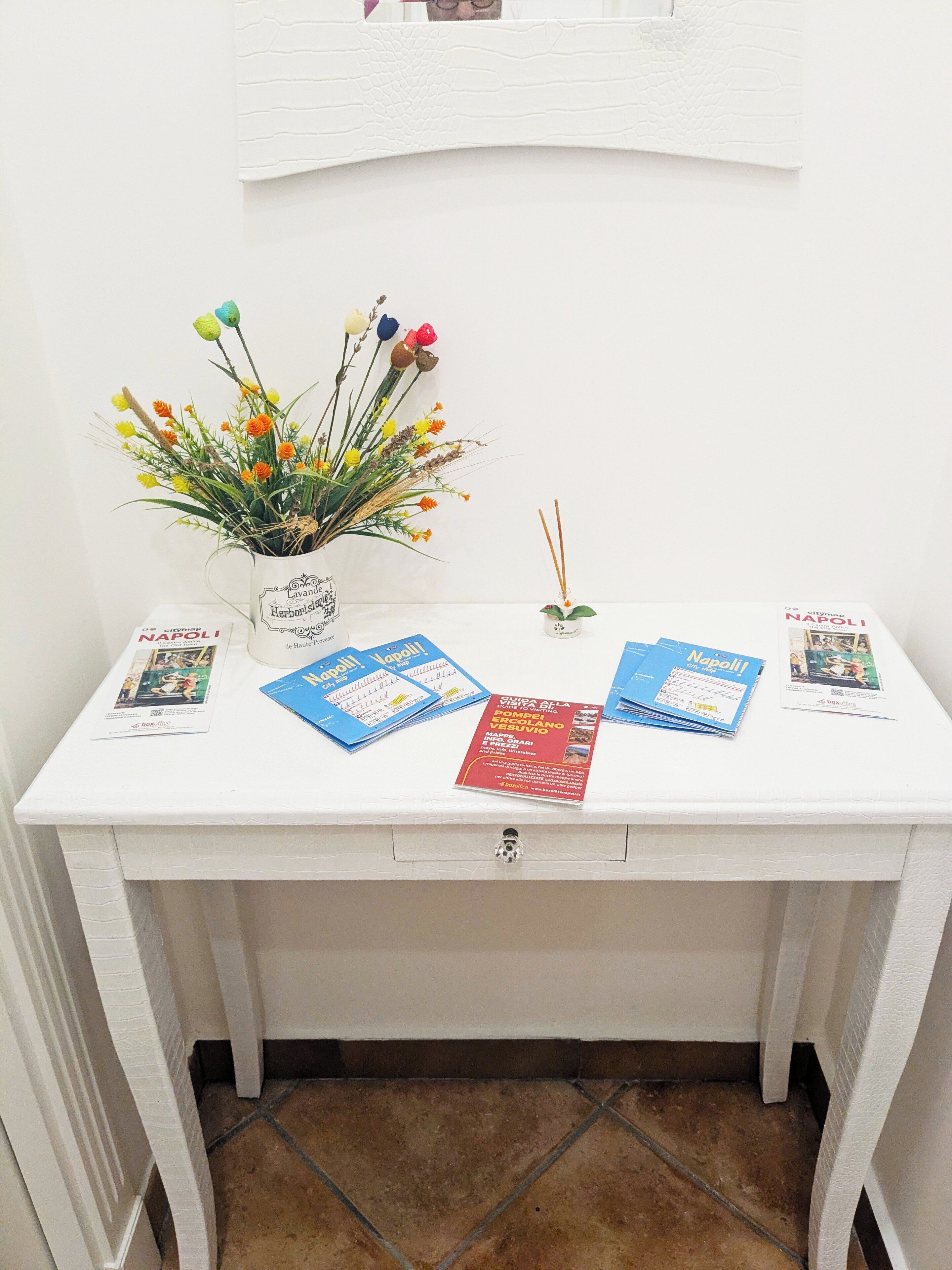 A white desk with a vase of colorful flowers, a few brochures, and a small decorative item.