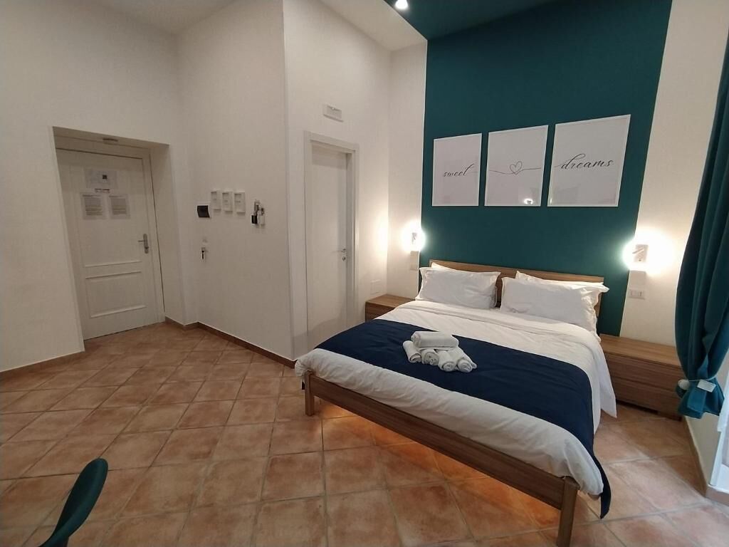 A bedroom with a bed, a nightstand, a wall-mounted light, and a door with a sign.