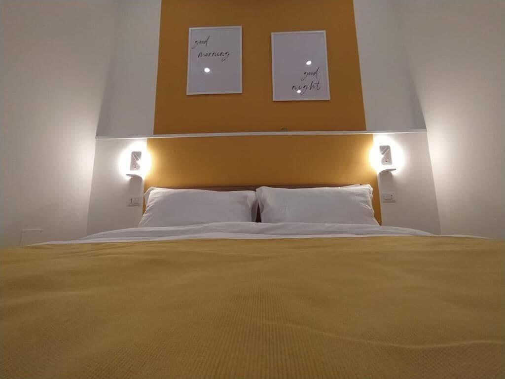 A hotel room with a bed, two bedside lamps, and two framed signs on the wall.