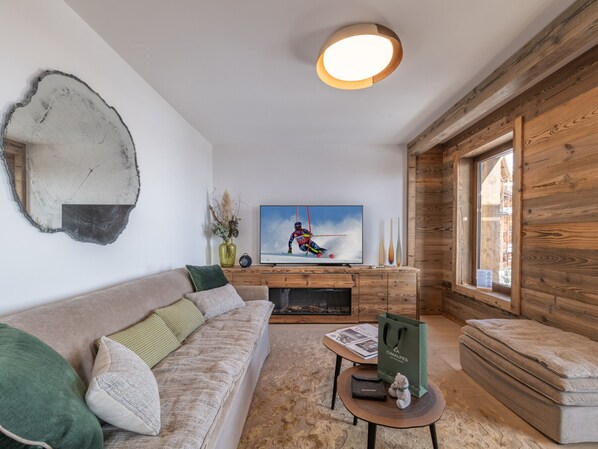 A modern living room with a sofa, coffee table, and a television displaying a skier. - High-end apartment in central location, up to 8 people (Huez)