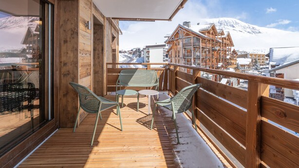 A wooden deck with a table and chairs, overlooking a snowy mountain and buildings. - High-end apartment in central location, up to 8 people (Huez)
