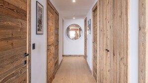 A hallway with wooden doors, a circular mirror on the wall, and framed pictures. - High-end apartment in central location, up to 8 people (Huez)