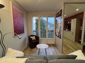 A cozy living room with a sofa, a chair, a small table, and a balcony with a view of trees and a fence. - Charming T2 with Balcony and Garage in Le Lioran (Le Lioran)