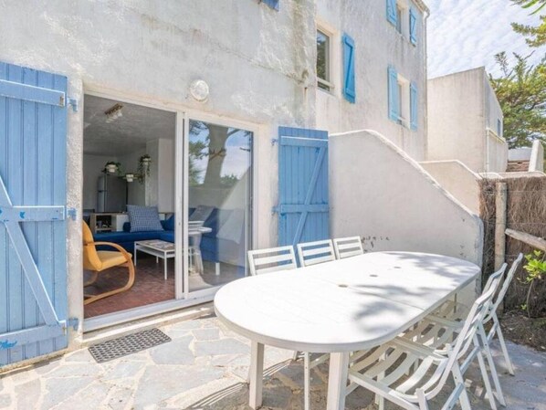 Un bâtiment doté d’un patio comprenant une table et des chaises blanches, un canapé bleu et un escalier.