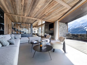 Ein modernes Wohnzimmer mit Holzboden, Steinwand und Blick auf schneebedeckte Berge.