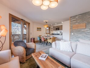 A modern living room with a sofa, a wicker chair, and a wooden coffee table. There is a dining area with a table and chairs, and a kitchen in the background. - Modern apartment in Morzine, 6 ppl, Wi-Fi, parking, near slopes (Morzine)
