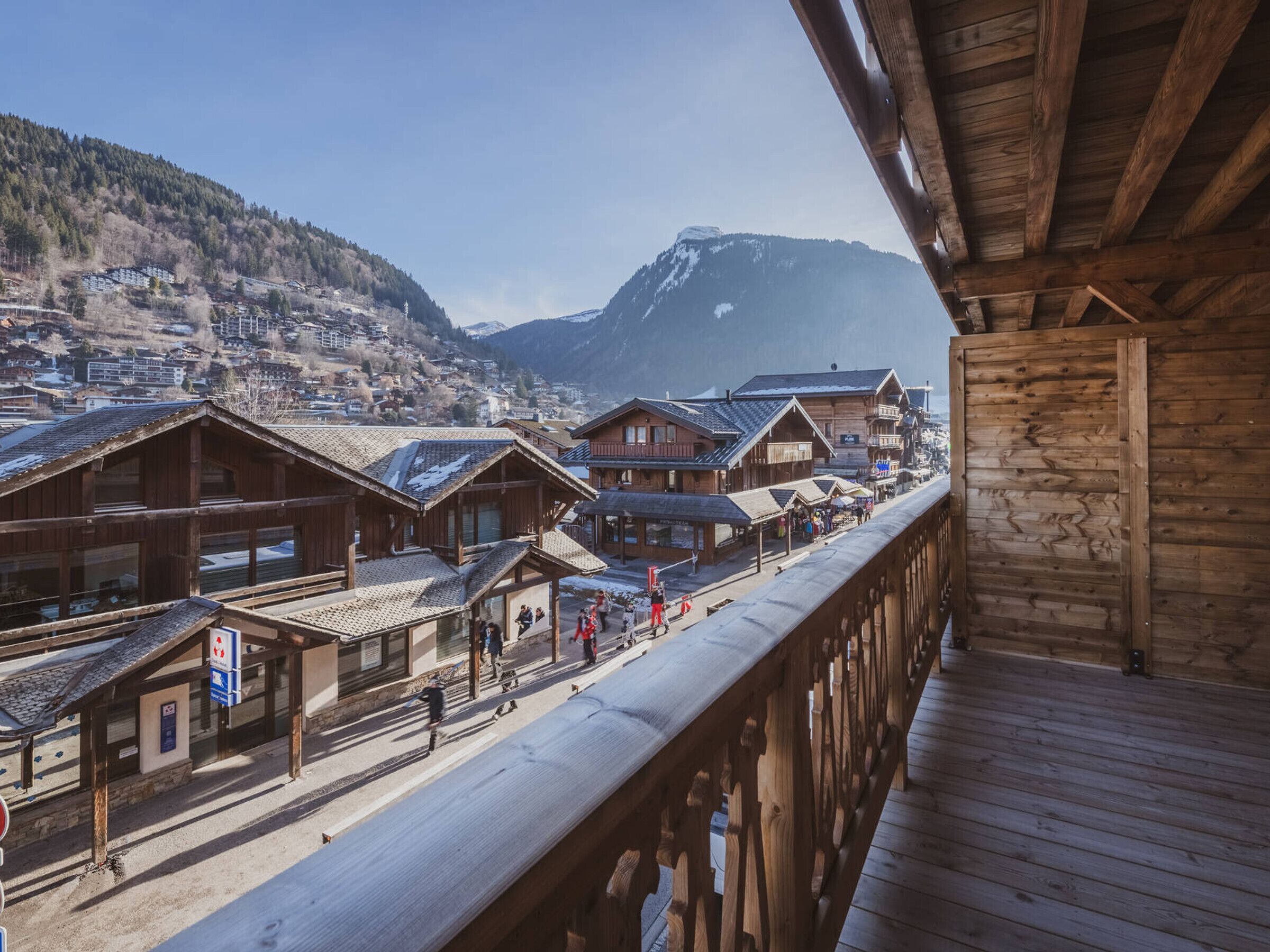 Edificio de madera con balcón que da a un pueblo nevado con casas tradicionales y una montaña al fondo.