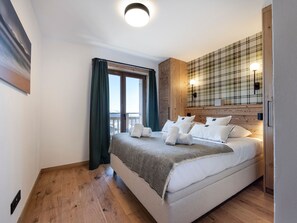 A bedroom with a bed, a window with curtains, a plaid-patterned wall, and a wooden floor. - Modern 3-bedroom apartment in La Rosière center (Montvalezan-La Rosière)