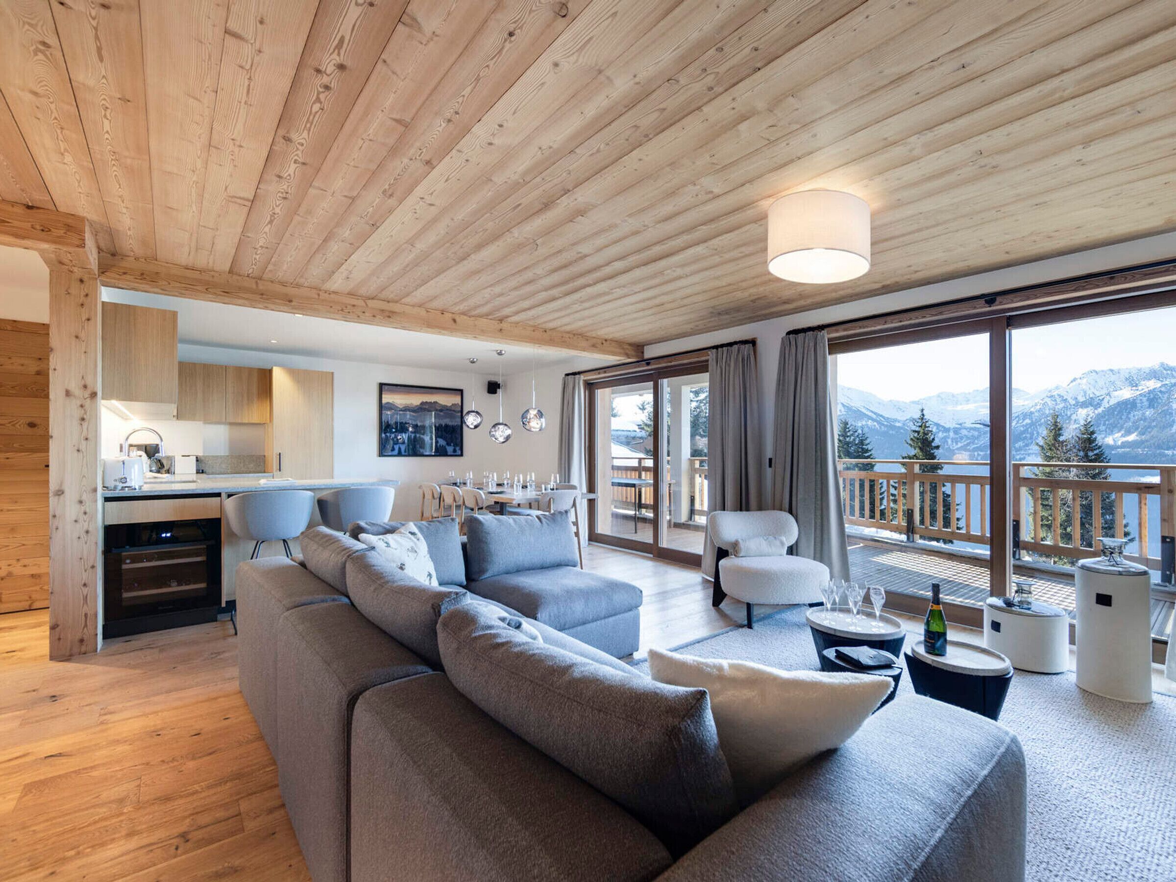 A modern interior with a wooden ceiling, a dining area, a sofa, and a view of mountains.
