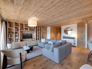 Ein modernes Wohnzimmer mit grauem Sofa, Holzregalen, einem Fernseher und einem runden Spiegel.