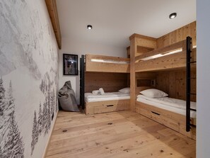 Ein Schlafraum mit Etagenbetten, Holzwänden, einem gerahmten Bild an der Wand und einer großen Tasche auf dem Boden.