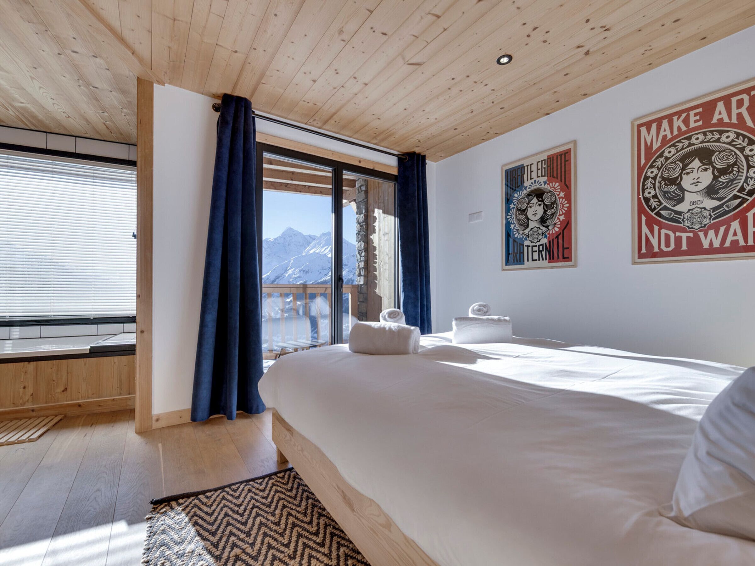 Une chambre avec un grand lit, une vue sur les montagnes et deux affiches accrochées au mur.