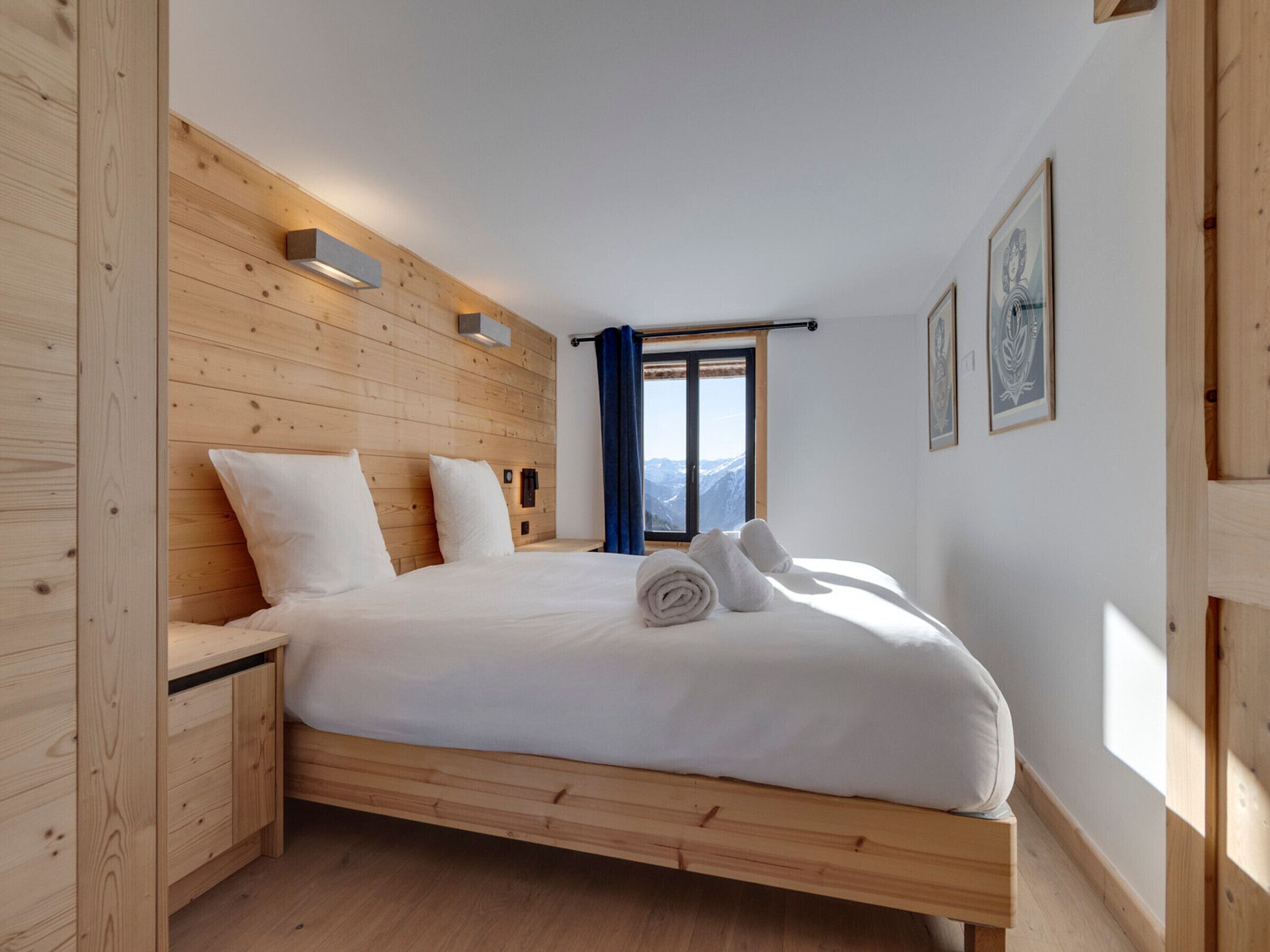 A wooden-paneled bedroom with a bed, a nightstand, and a window with a view of mountains.