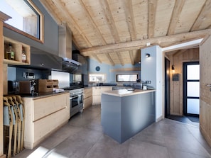 Une cuisine moderne avec des poutres en bois, un îlot central, des appareils électroménagers intégrés et une grande fenêtre.