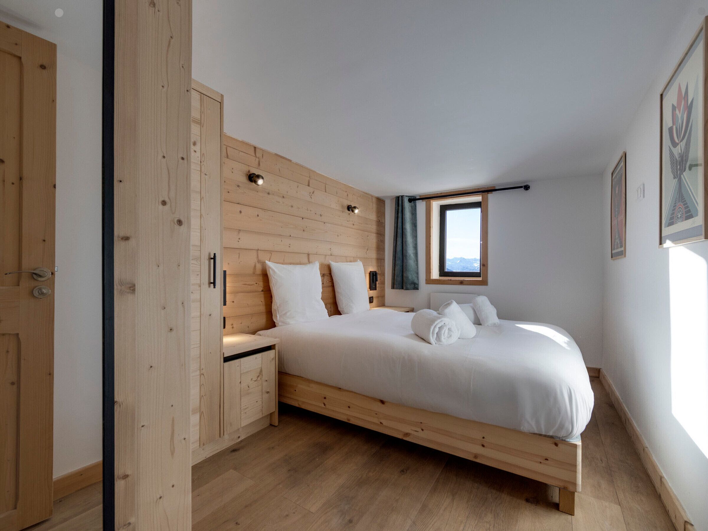 Une chambre à coucher avec une tête de lit en bois, un lit simple avec du linge de lit blanc, une table de chevet, une armoire en bois, une fenêtre avec vue et un tableau encadré au mur.