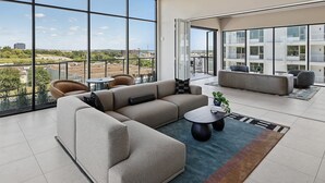 Un salon moderne avec un canapé d’angle, une table basse ronde et une vue sur la ville grâce à de grandes fenêtres.