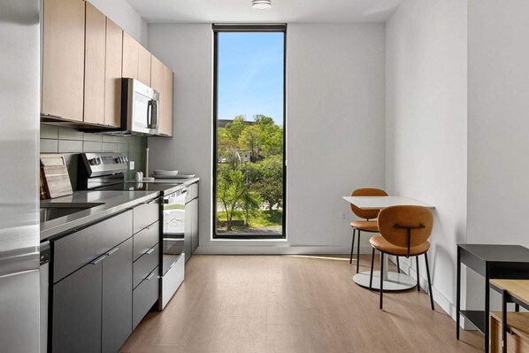 Una cocina moderna con un ventanal grande, armarios de madera y una zona de comedor con dos sillas.